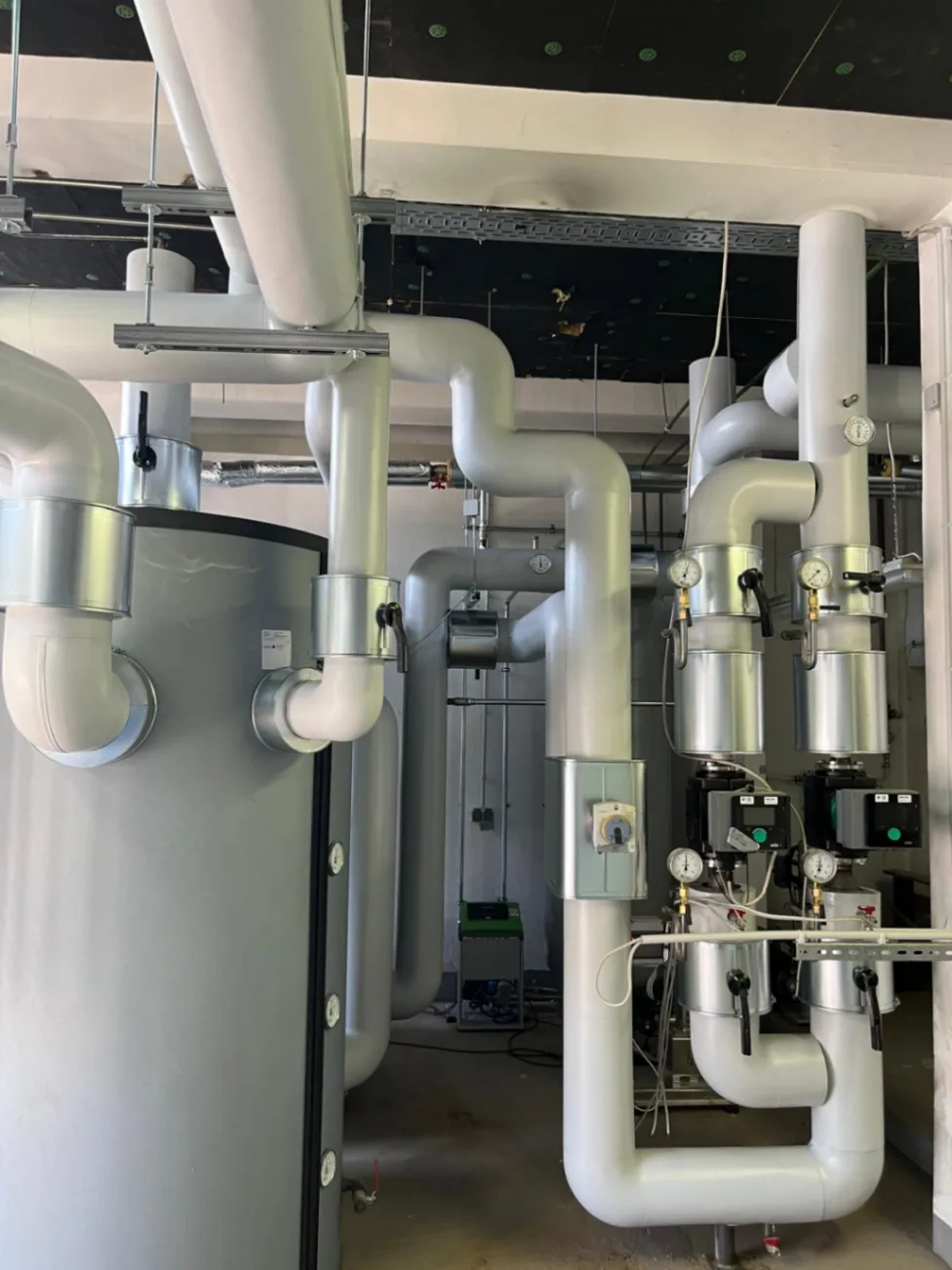Gedämmte Technikzentrale mit isoliertem Pufferspeicher, weißen Rohrleitungen und Pumpen